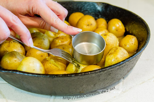 Smashing small potatoes with a fork and a metal measuring cup.