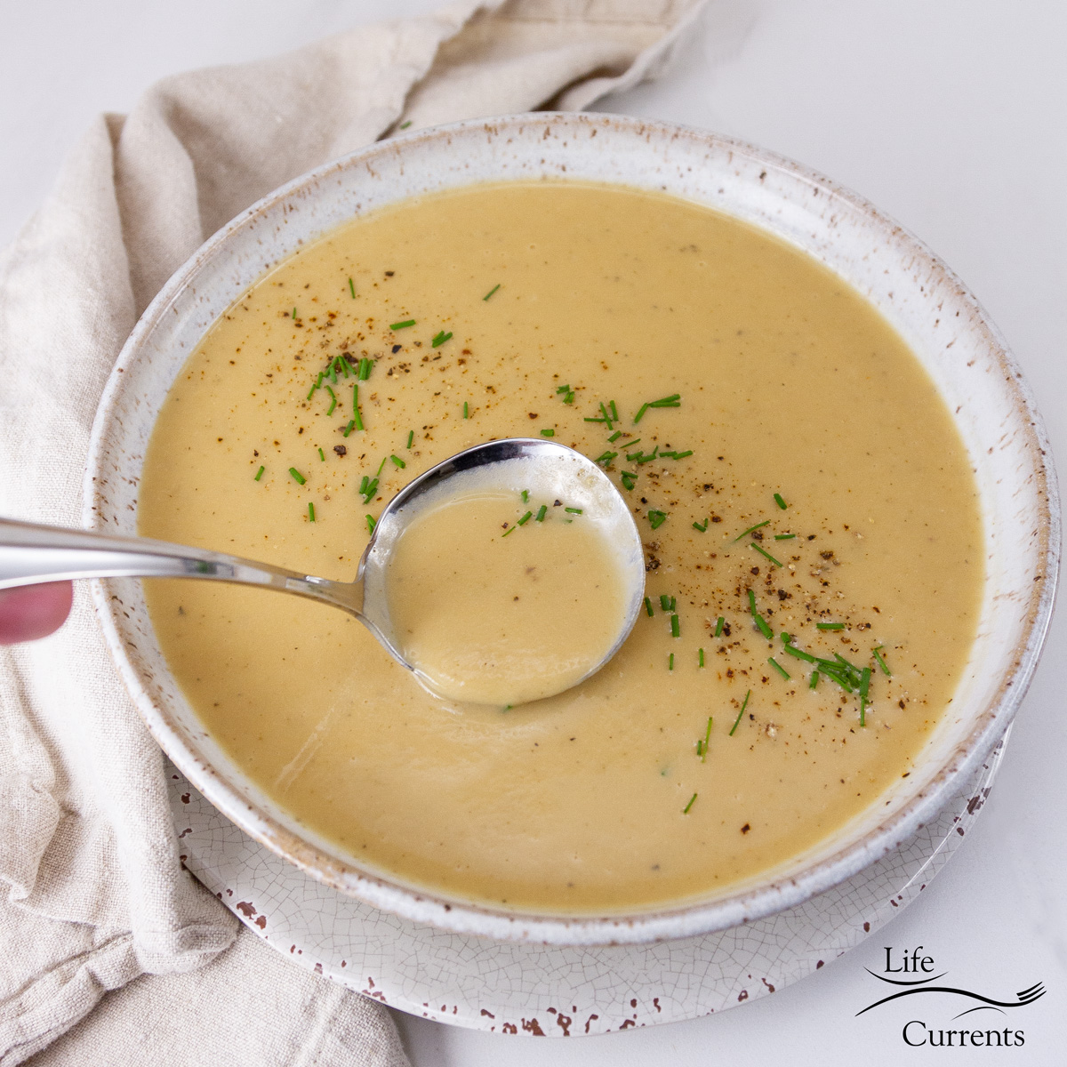 square crop of a bowl of soup being served with a ladle.