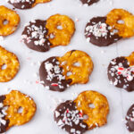square crop of pretzel crisps dipped in chocolate and sprinkled with crushed peppermint candies on a piece of parchment paper.