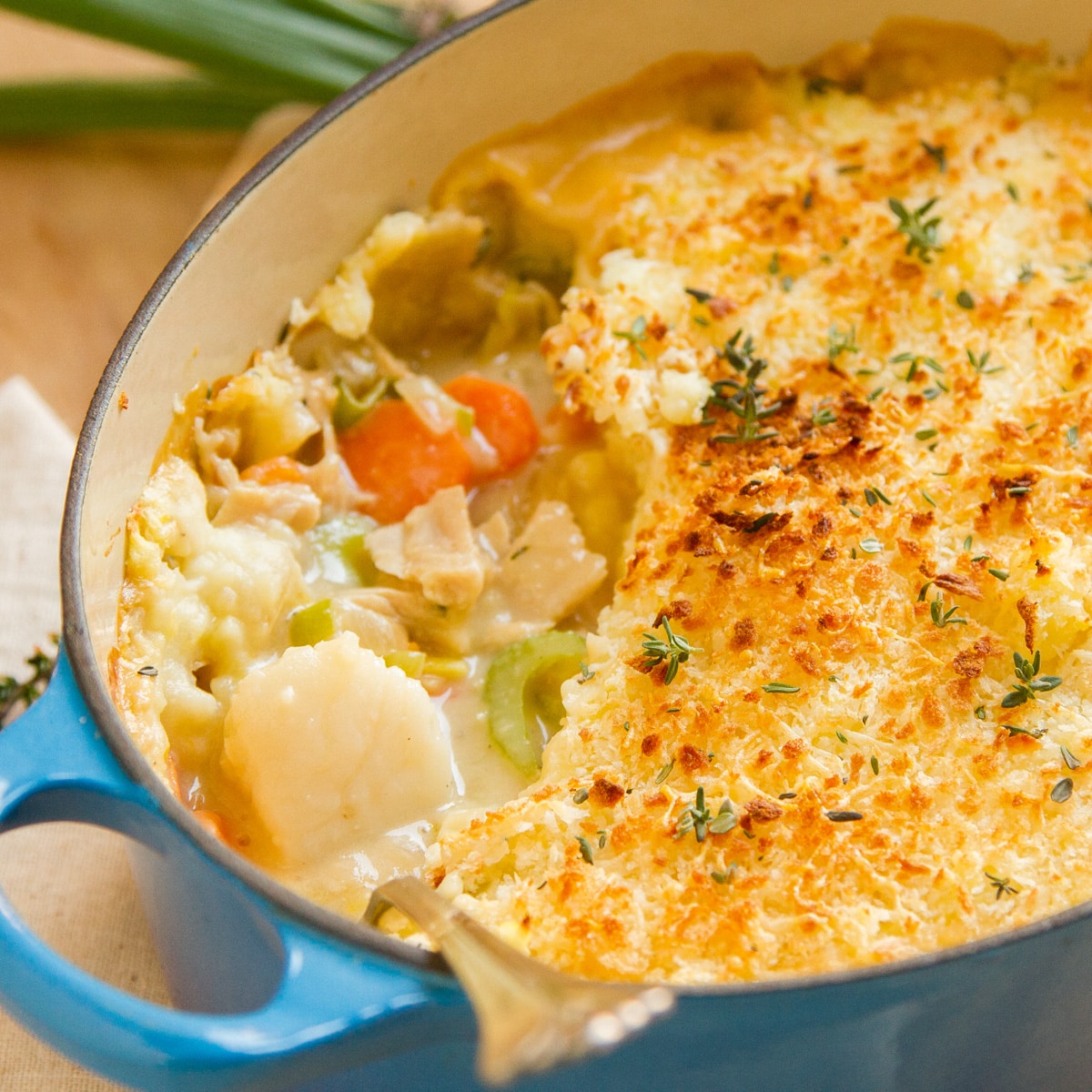 a blue casserole dish filled with Seafood Shepherd&rsquo;s Pie that's garnished with thyme, green onions in the background.