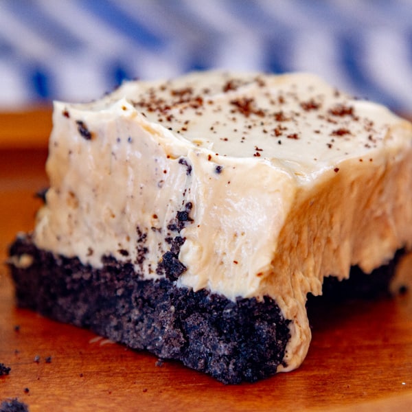 close up on a cheese cake piece with cookie crust and there's a blue and white striped cloth in the background.