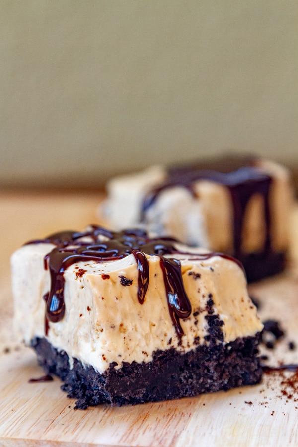 two pieces of cheesecake on a wooden serving plate drizzled with chocolate sauce.
