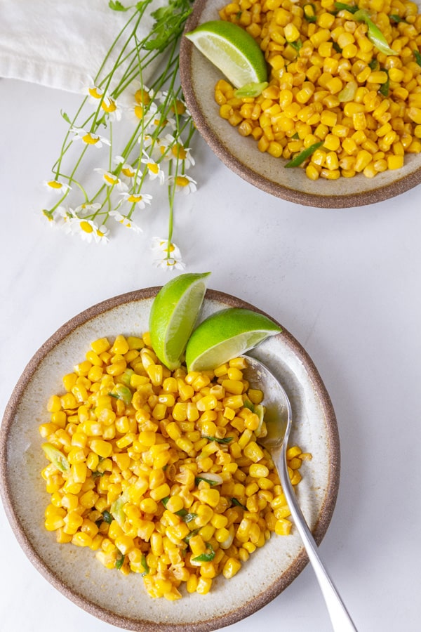 Two bowls of corn with lime wedges and some flowers next to the bowls.