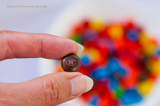 Football Party Dessert Spread including Pie Crust Cookies with M&M'S® Brand Milk / Peanut Chocolate Candies Game Day Mix - this is the perfect easy way to entertain during football season a hand holding a single M&M.
