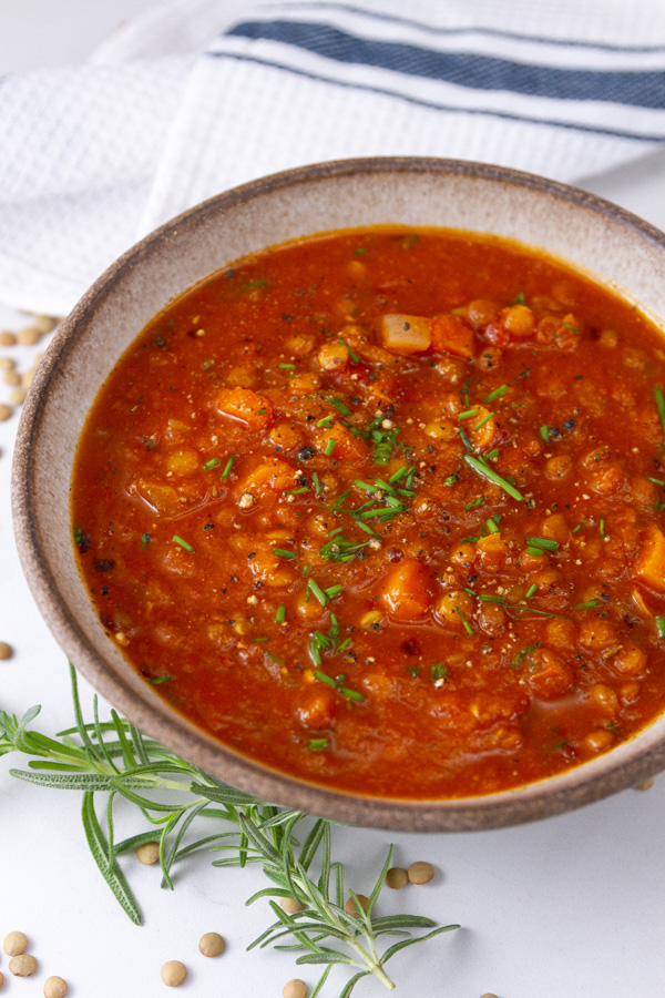 a bowl of tomato soup with lots of veggies garnished with herbs next to a blue striped towel.