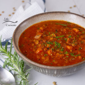 square crop of a bowl of soup with fresh herbs and a towel next to it.