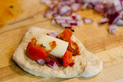 the circle of dough, topped with sauce, cheese, red pepper and red onions.