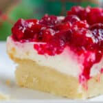 close up on a dessert bar with an almond cookie crust, cheesecake layer, and topped with cranberry sauce.