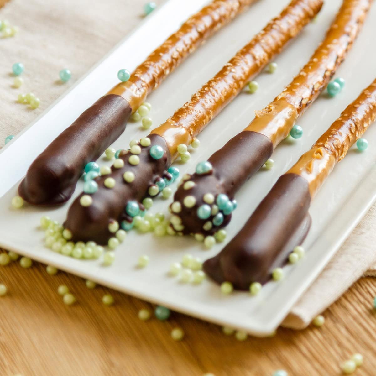 4 pretzel rods that have been dipped in chocolate on a white plate.