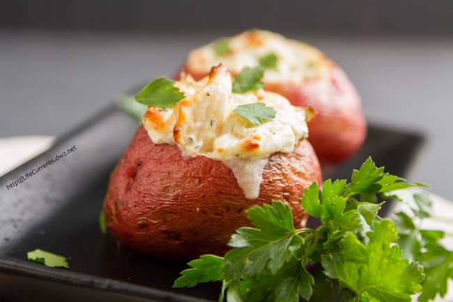 two red potatoes stuffed with creamy crab filling and garnished with fresh parsley on a black plate.