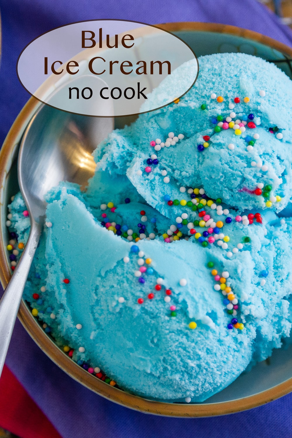 a small bowl of blue ice cream topped with colorful sprinkles and a spoon on the left of the bowl.