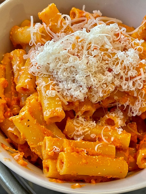 ziti pasta with red pepper and feta sauce topped with shredded Parmesan cheese.