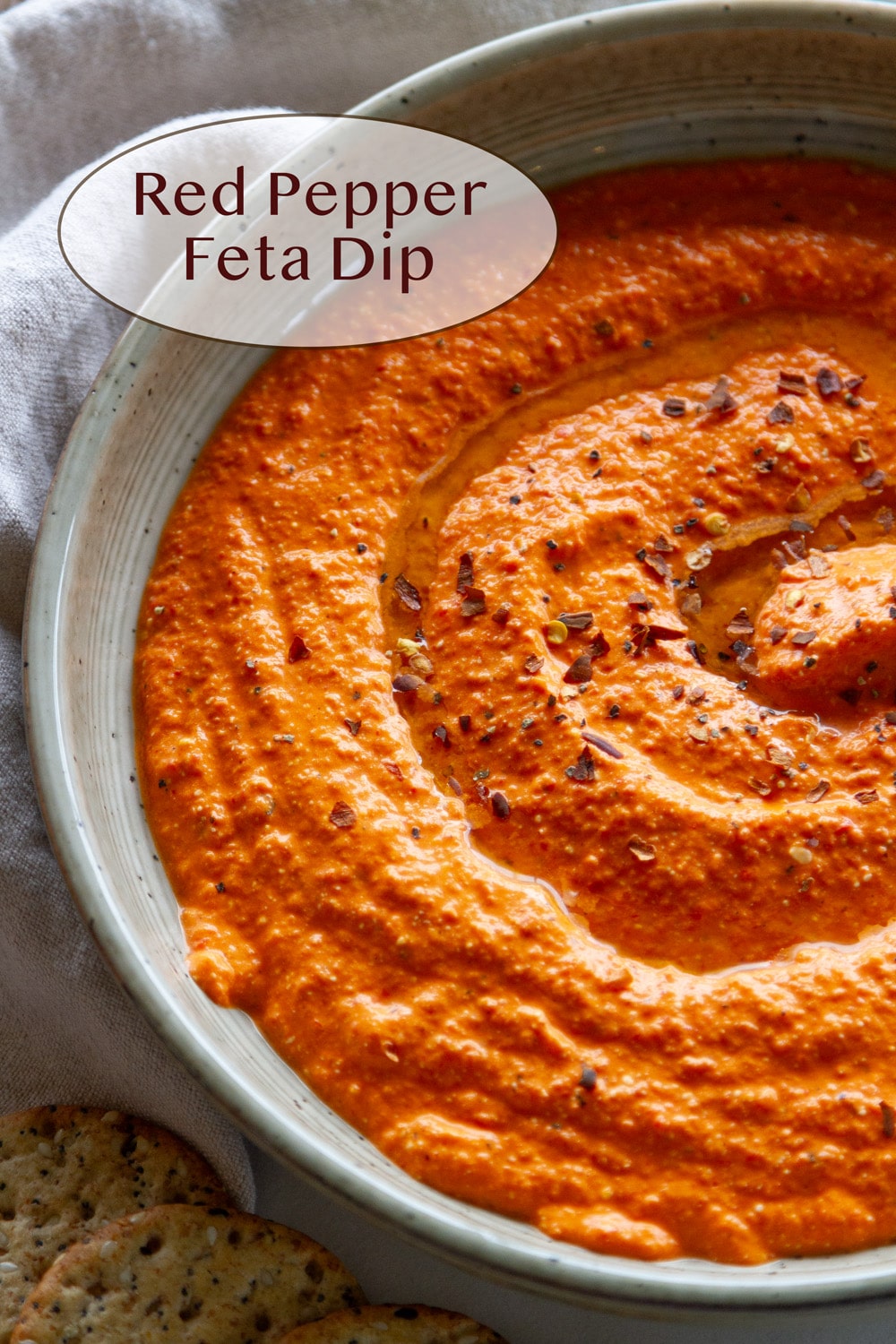 Red Pepper Feta Dip that's creamy and swirled in a bowl topped with red pepper flakes and pepper and olive oil.