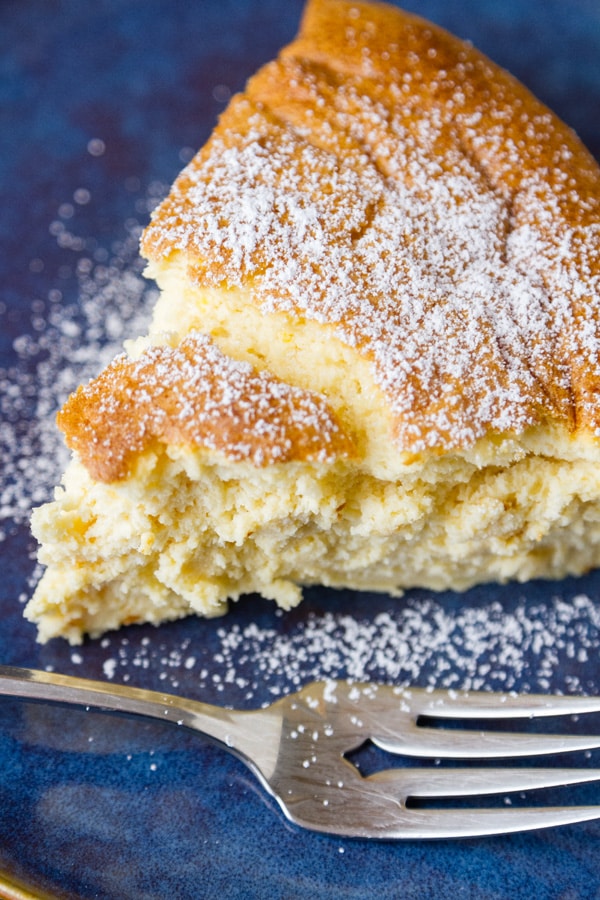 looking down on a slice of cheesecake that's dusted with powdered sugar on a blue plate and a fork in the lower area.