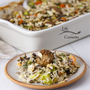 square crop of wild rice and broccoli casserole on a plate in front of the casserole dish.
