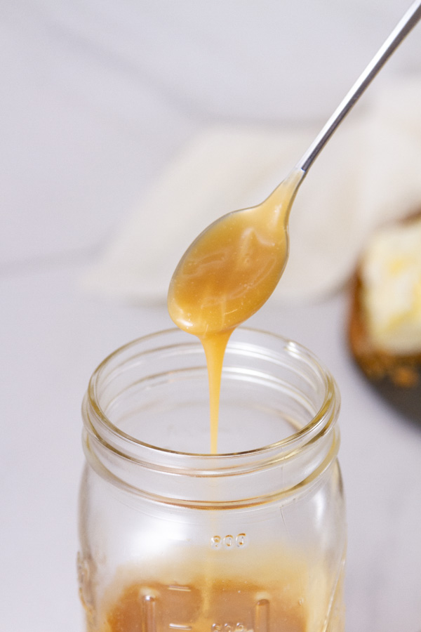 a spoon pouring caramel sauce into a mason jar.