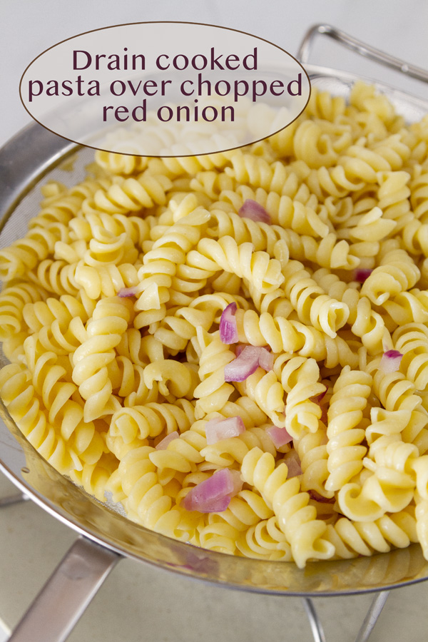 cooked pasta with red onions in a strainer.