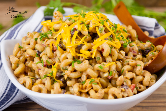 pasta salad in a white bowl topped with cheddar cheese.