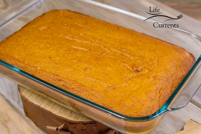 the cake in a glass 13 by 9 inch pan cooling on a wooden stand. 