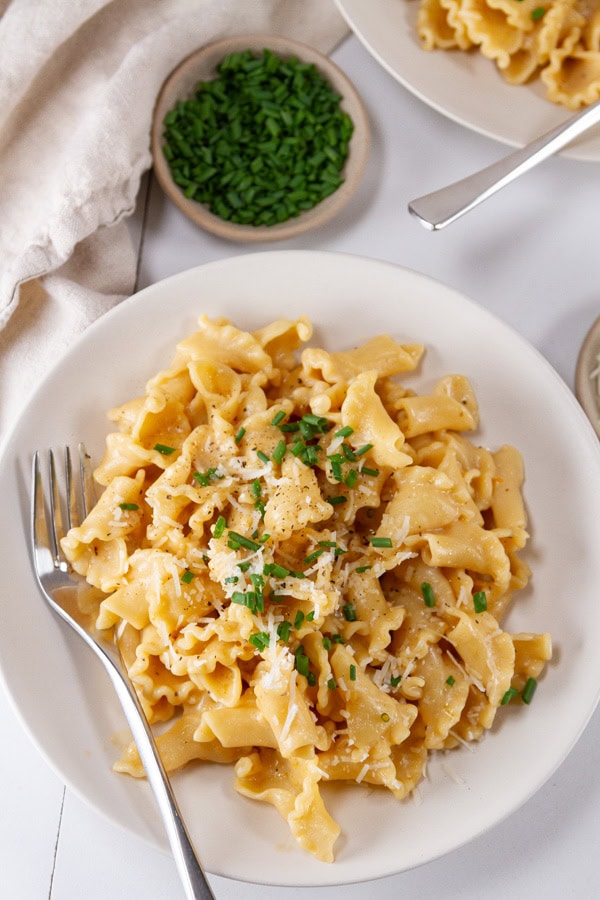 A bowl full of pasta with a fork in it and a small dish of chives in the upper left.