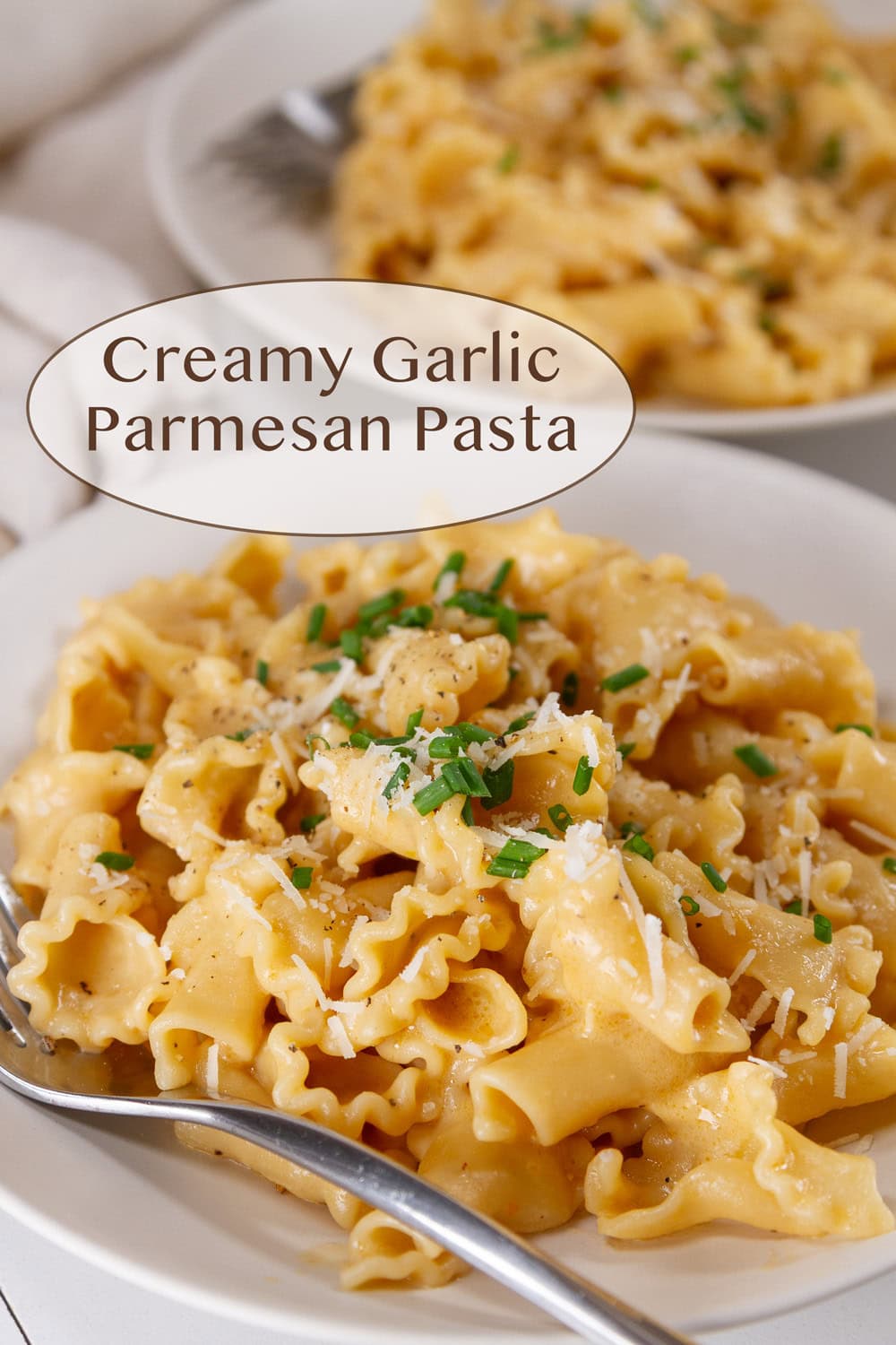 a bowl full of pasta in creamy sauce topped with chives and a fork in the bowl.