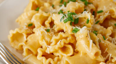 square crop of a bowl of pasta in creamy garlic sauce topped with chives and a fork in the bowl.
