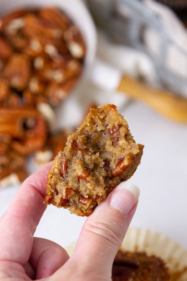 A muffin with a big bite taken out of it so you can see the inside in front of a measuring cup full of pecans.