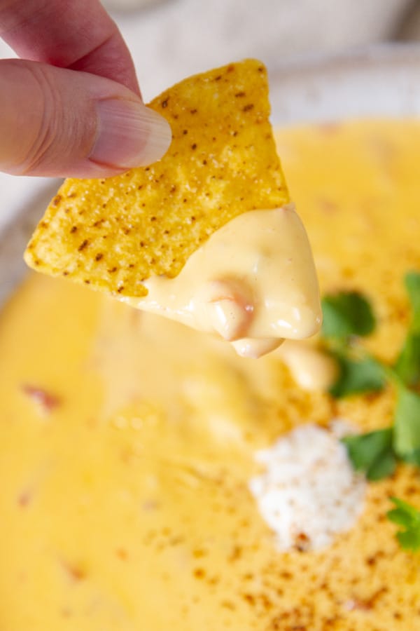 a chip dipped into cheese sauce with the bowl of cheese sauce in the background.