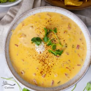 looking down on a bowl of nacho cheese dip that's garnished with sour cream and cilantro.