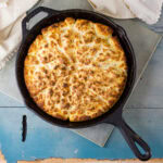 looking down on a cast iron skillet with biscuits baked inside on a blue background.