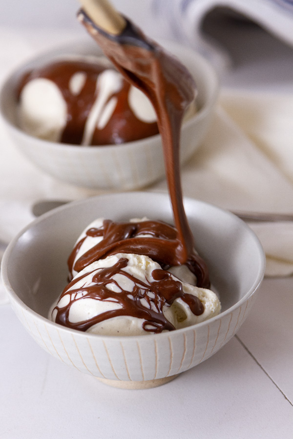 spooning hot fudge sauce over ice cream