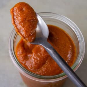a glass jar filled with BBQ sauce and a spoon on top holding a spoonful of the thick sauce.
