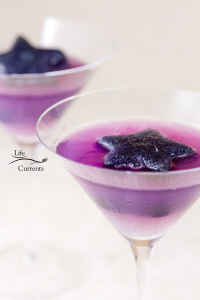 two cocktail glasses filled with purple lemonade and a purple ice star floating on top.