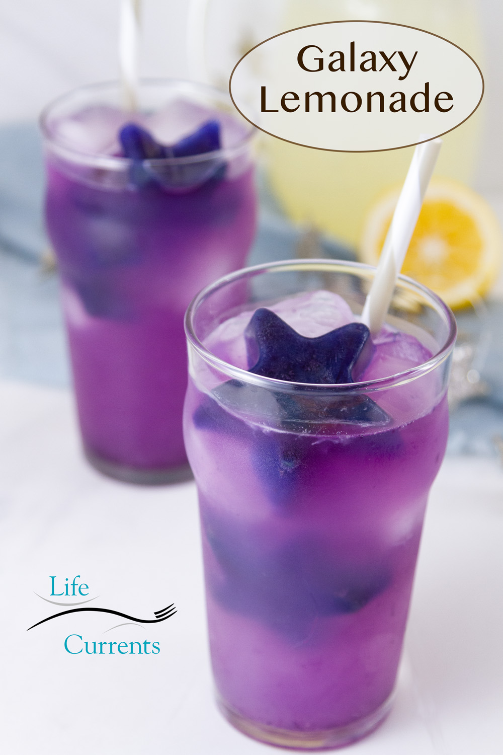 two glasses filled with lemonade and purple stars, straws, and a pitcher of lemonade behind.