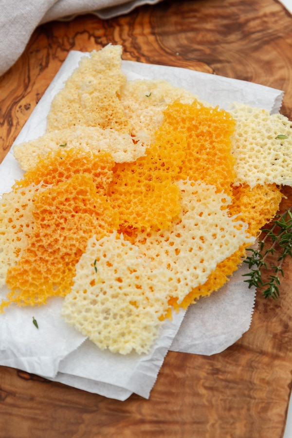 several pieces of crispy cheese stacked on a piece of parchment paper.