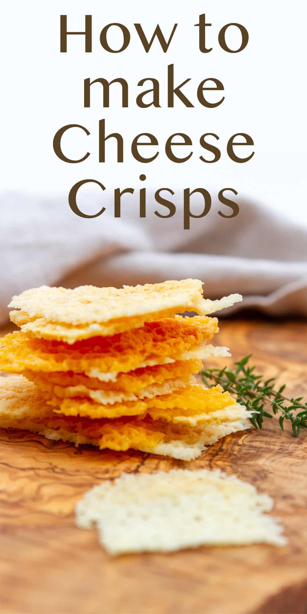a stack of small pieces of cheese crisps with different kinds of cheese on a wood board with fresh thyme next to the stack.