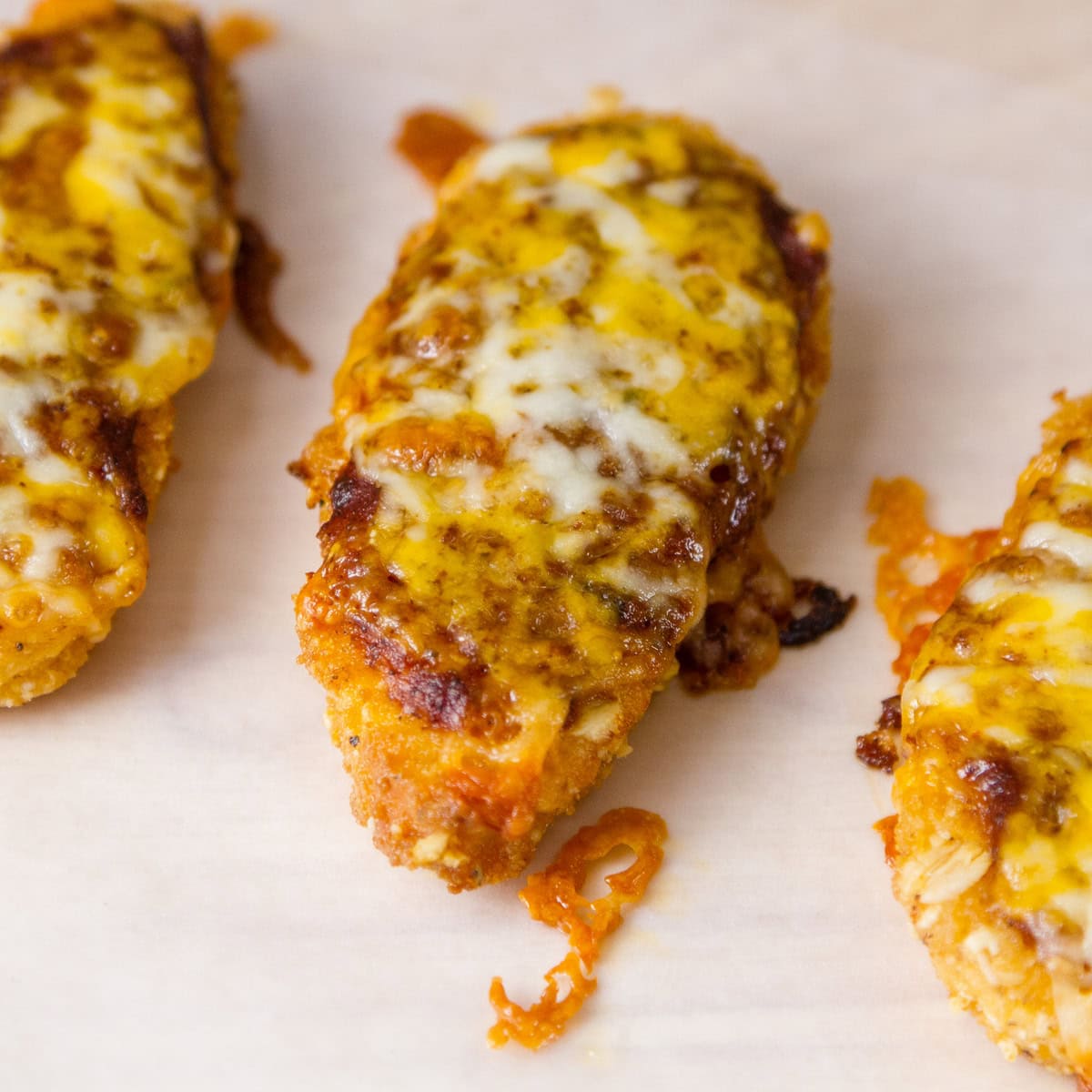 three chicken tenders topped with red sauce and cheese.