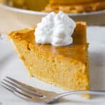 I slice of sweet potato pie with a dollop of whipped cream on top and a fork in front.