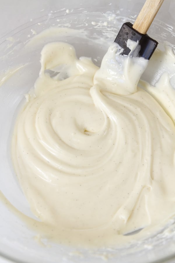 cream cheese icing in a glass bowl with a black spatula.