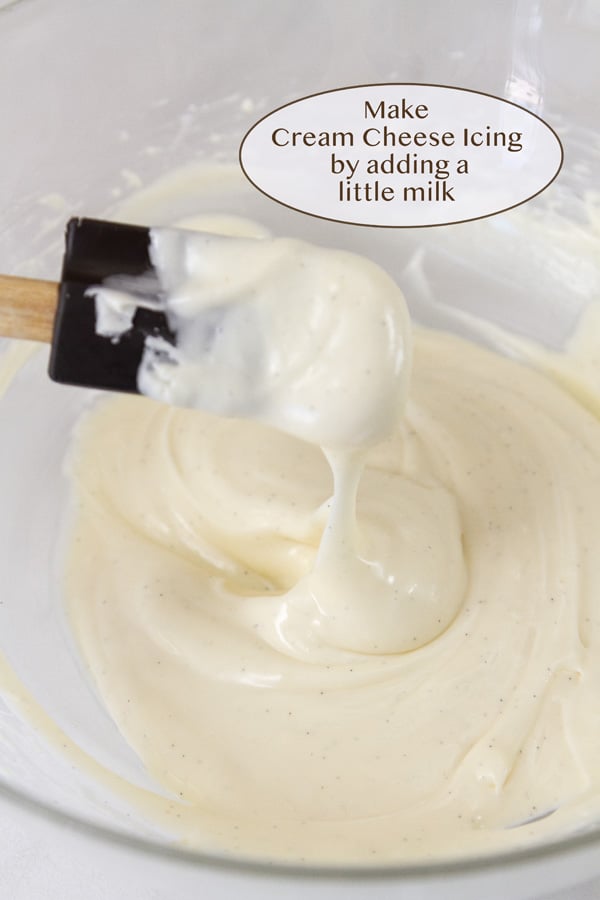 a bowl with cream cheese icing being drizzled with a spatula.
