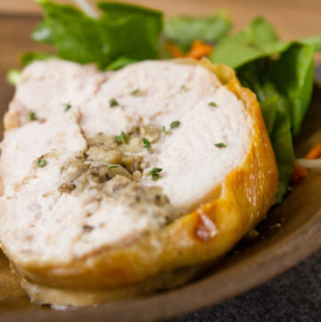 A slice of cooked turkey rolled around stuffing on a plate with salad behind it.