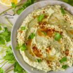 looking down into a bowl of green hued hummus with spice and cilantro on top.