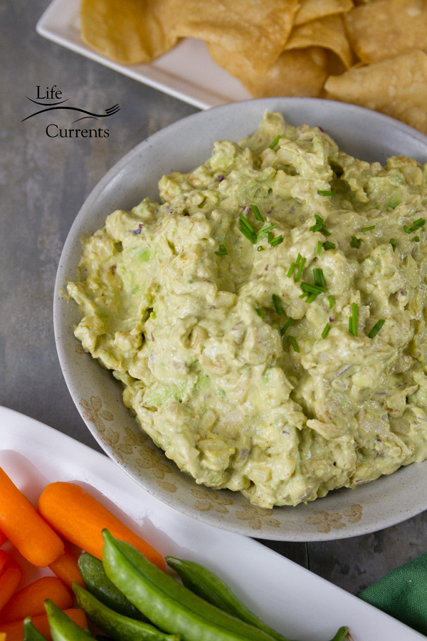 Chipotle Corn Guacamole appetizer for your next game watching party - guacamole in a grey bowl served with chips, baby carrots, and snap peas