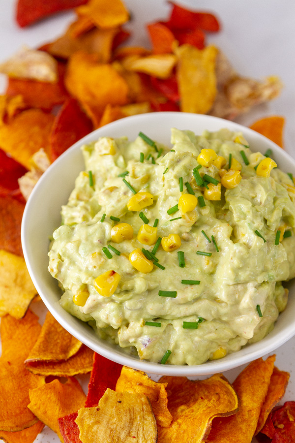 a bowl of guacamole dip surrounded by vegetable chips.