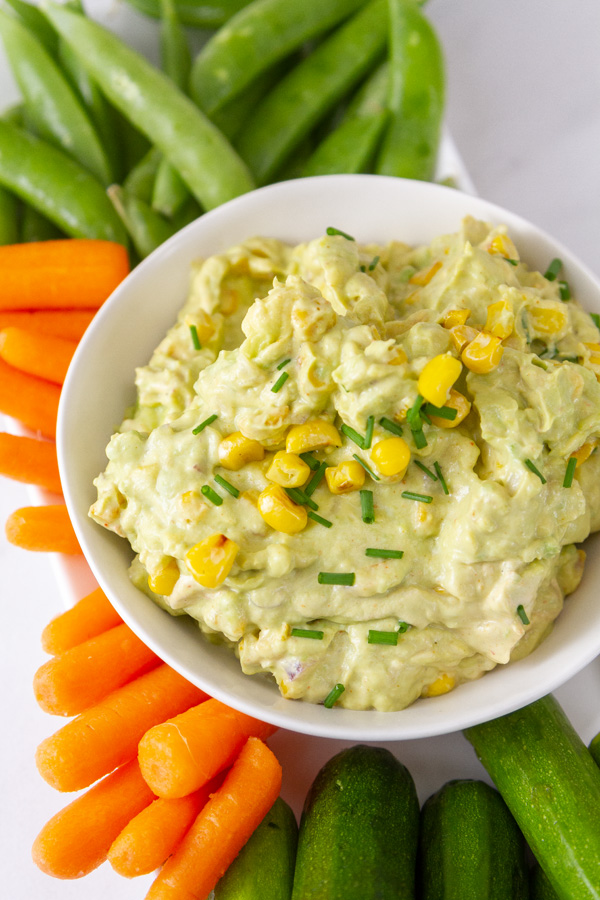 a bowl of guacamole with baby carrots, snap peas, and baby zucchini around it.