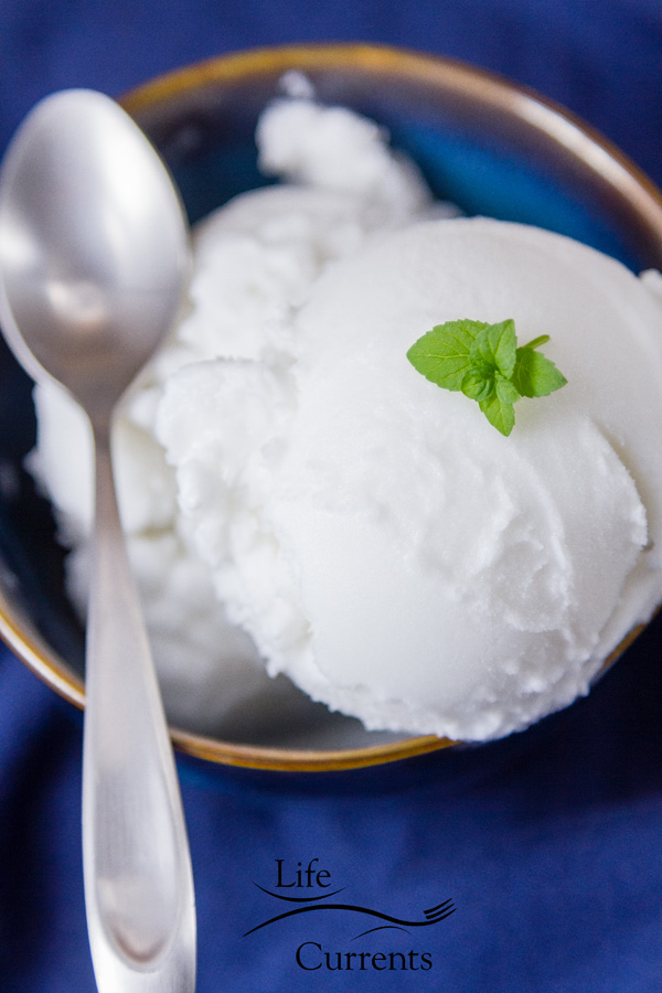 creamy and delicious white coconut sorbet scooped high in a blue bowl with a silver spoon and a mint leaves for garnish 