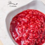 Square crop of the featured image of the bright red roasted raspberry sauce in a small white dish on a white background