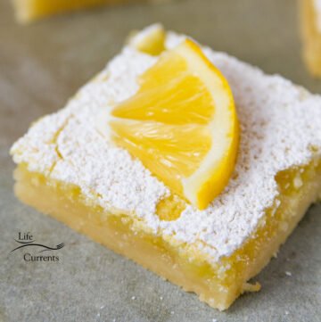 close up on a lemon bar slice with a lemon garnishing the top