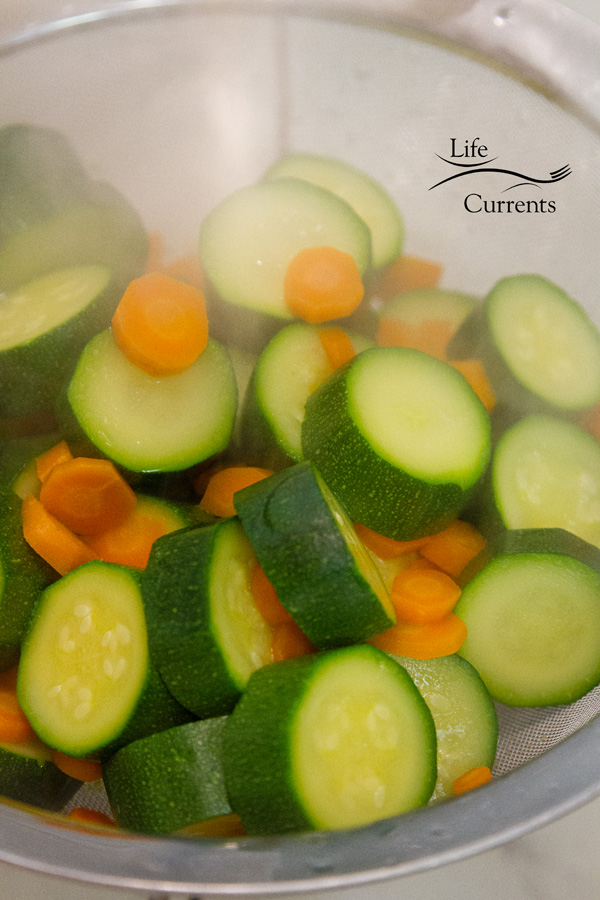 Zucchini and carrots lightly boiled and draining in a strainer with steam coming off of them