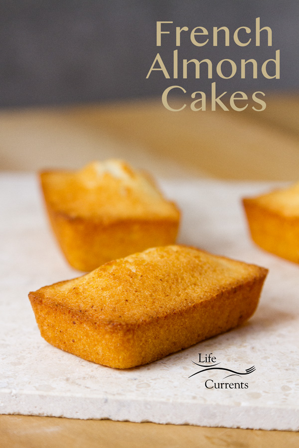 Three Financiers (French Almond Cakes) on a white napkin with a wood platform and a grey background 